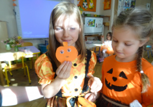 Dwie inne dziewczynki siedzą obok siebie z papierowymi dyniami.