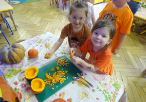 Dwie dziewczynki siedzą przy stole i sprawdzają pestki dyni.