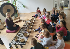Dzieci siedzą na podłodze podczas warsztatów przed prowadzącą warsztaty.