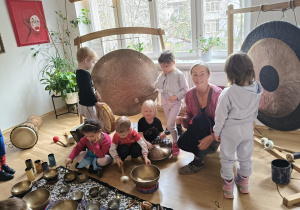 Dzieci podczas zabawy instrumetami w towarzystwie osoby prowadzącej warsztaty.