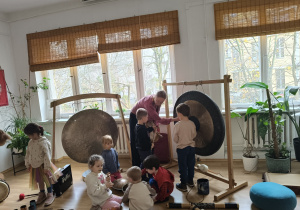 Inna grupa dzieci podczas zabawy instrumetami w towarzystwie osoby prowadzącej warsztaty.