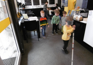 Chłopiec trzyma laskę i idzie przez salę.