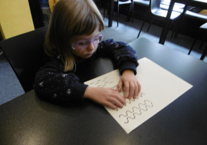 Dziewczynka trzyma ręce na kartce z wypukłymi kształtami.