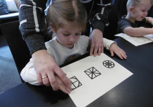 Inna dziewczynka dotyka wypukłych kształtów na kartce papieru.