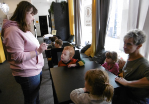 Dzieci oglądają przedmiot trzymany przez prowadzącą warsztaty.