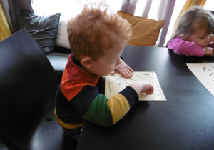 Chłopiec palcem dotyka kartki z wypukłymi kształtami.