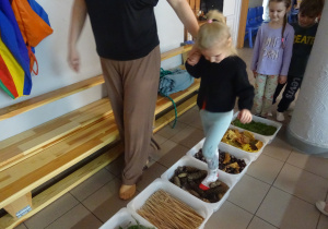 Dziewczynka idzie drogą zbudowaną z róznych materiałów.