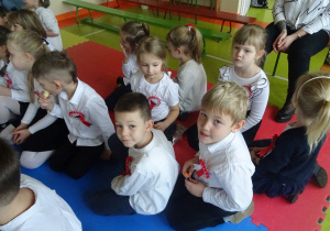 Grupa dzieci siedzina materacach w sali szkolnej.