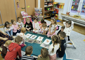 Dzieci siedzą na dywanie i przeglądają ilustracje.