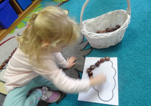 Dziewczynka układa kasztany na ciemnej lini.