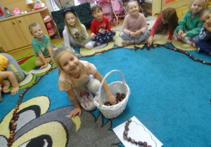 Dziewczynka wkłada kasztan do koszyczka.