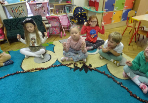 Dzieci siedzą na dywanie i mają zamknięte oczy.