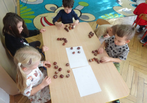 Dzieci układaja kasztany na kartce.