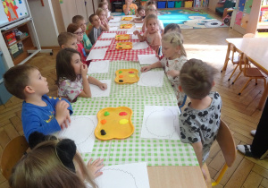 Dzieci siedzą przy stole i przygotowują się do malowania.