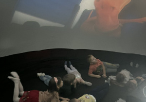 Dzieci leżą i obserwują ekran.