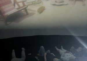 Dzieci leżą jeden obok drugiego i oglądają bajkę na ekranie.