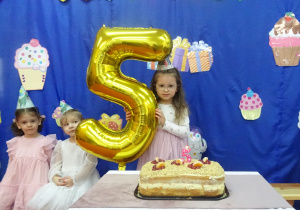 Dziewczynka stoi z balonem w kształcie cyfry pięć.