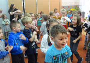 Grupa dzieci stoi na dywanie obok siebie.