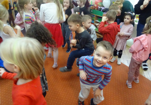 Grupa dzieci stoi na dywanie podczas wspólnych zabaw.