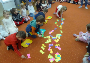 Grupa dzieci układa kolorowe rybki na dywanie.