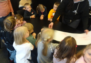 Inna grupa dzieci trzyma w górze biały karton papieru.