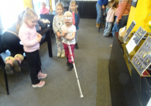 Inna dziewczynka idzie trzymając przed sobą laskę.