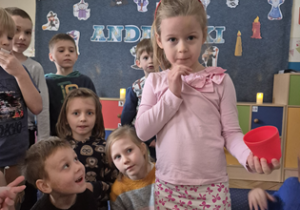 Dziewczynka stoi przed stolikiem z czerwonymi kubeczkami.