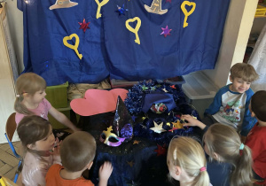 Dzieci stoją przy stoliku na którym są kolorowe paierowe gwizdy.