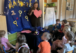 Nauczycielak trzyma przed sobą papierowe różowe serce.