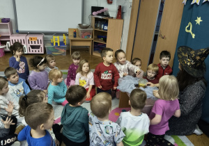 Dzieci siedzą na dywanie przed nauczycielem.
