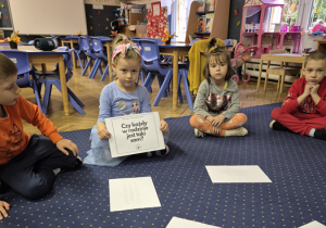 Dziewczynka siedzi na dywanie z planszą w ręku.