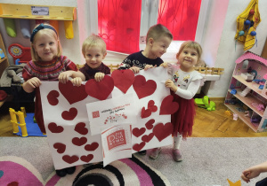 Inna grupa dzieci stoi z plakatem z papierowymi sercami.