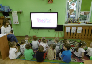 Dzieci siedzą przed monitorem z prezentacją multimedialną.