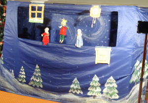 Trzy lalki stoją w oknie domu z papieru.