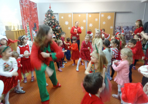 Dzieci tańczą w spólnie na sali przedszkolnej.