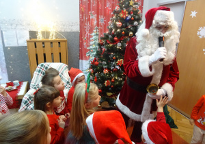 Mikołaj trzyma w ręku Mikrofon i mówi do grupy innych dzieci.