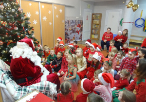 Dzieci siedzą na dywanie przed Mikołajem.