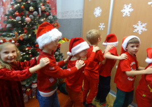 Grupa dzieci stoi jedno za drugim i trzyma się za ramiona.