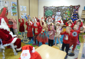 Dzieci stoją przed Mikołajem i unoszą ręcę do góry.