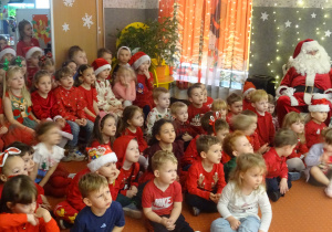 Dzieci i Mikołaj siedzą na dywanie.