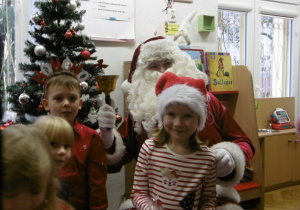 Mikołaj w otoczeniu dzieci siedzi na fotelu.