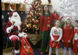 Dzieci stoją przy Mikołaju i osobie przebranej za Elfa.