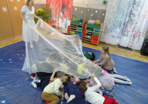 Grupa dzieci schowała się pod biała chustą.