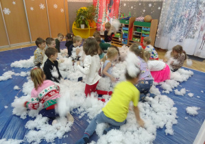 Dzieci i osoba prowadząca warsztaty siedzą na dywanie w puchu.