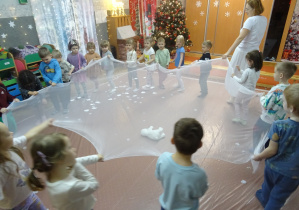 Grupa dzieci trzyma białą przezroczystą chustę.