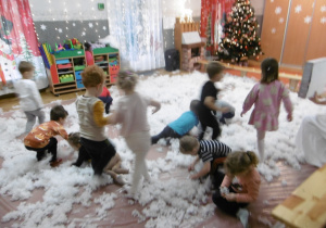 Dzieci bawią się w otoczeniu białego puchu.