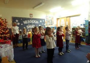 Dzieci podczas występu trzymają ręce na ramionach.