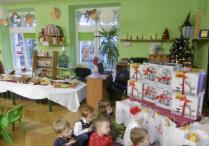 Dzieci w otoczeniu prezentów siedzą na dywanie.