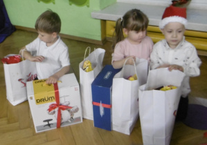 Troje dzieci siedzi przy prezentach.