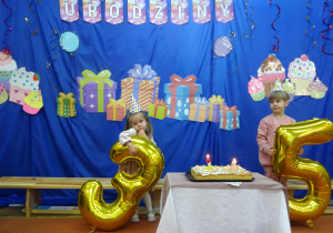 Dwoje dzieci stoi przy cieście urodzinowym.